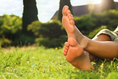 Photo of Woman sitting barefoot on green grass outdoors, closeup. Space for text