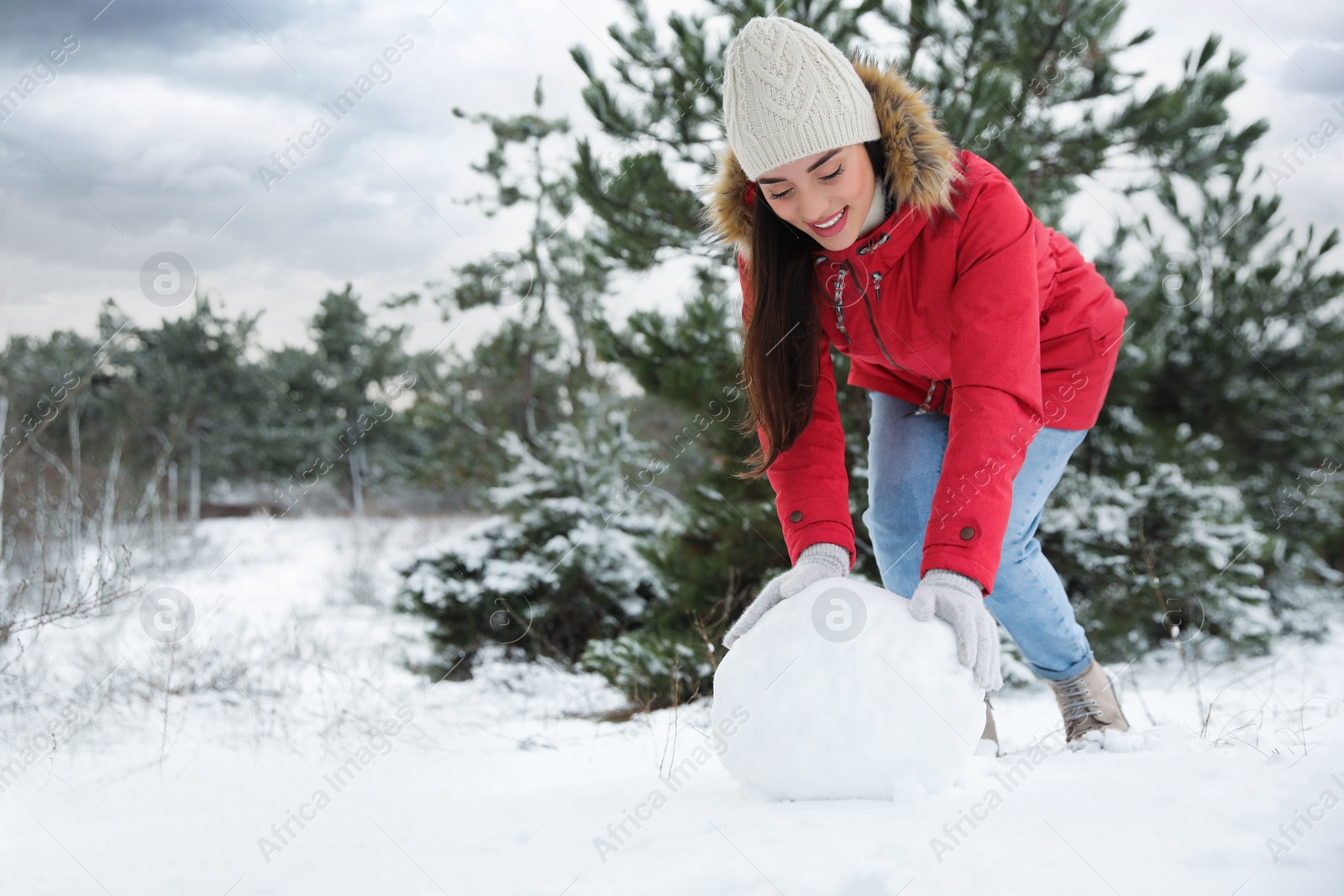 Photo of Young woman rolling snowball outdoors on winter day. Space for text