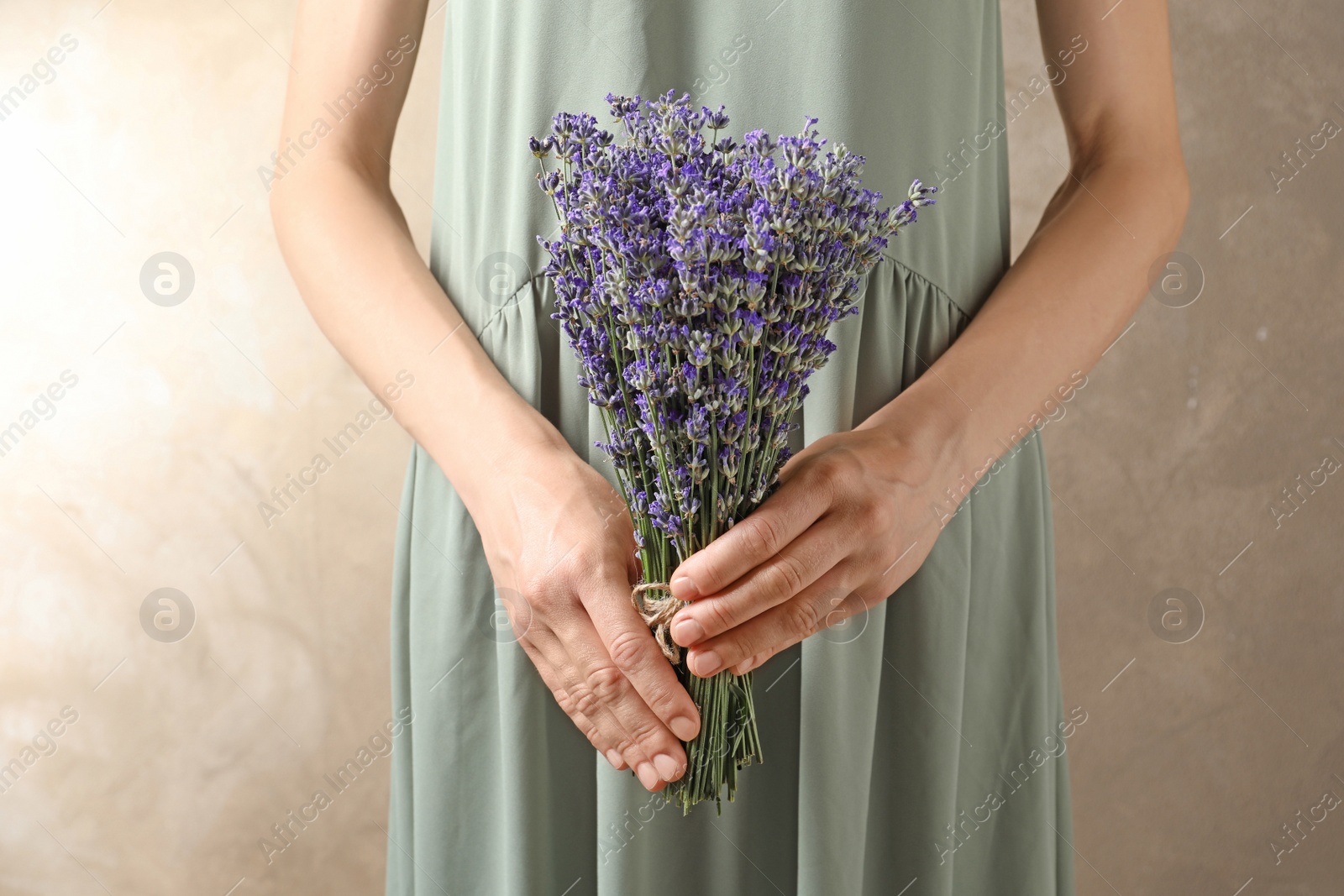 Photo of Woman holding fresh lavender flowers on beige background, closeup view