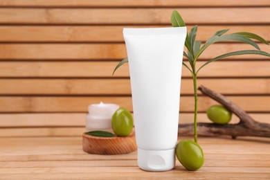 Photo of Tube of natural cream, olives and leaves on wooden table