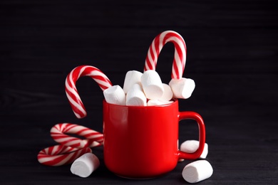 Photo of Cup of tasty cocoa with marshmallows and Christmas candy canes on black wooden table