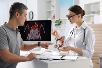 Gastroenterologist with anatomical model of large intestine consulting patient at table in clinic