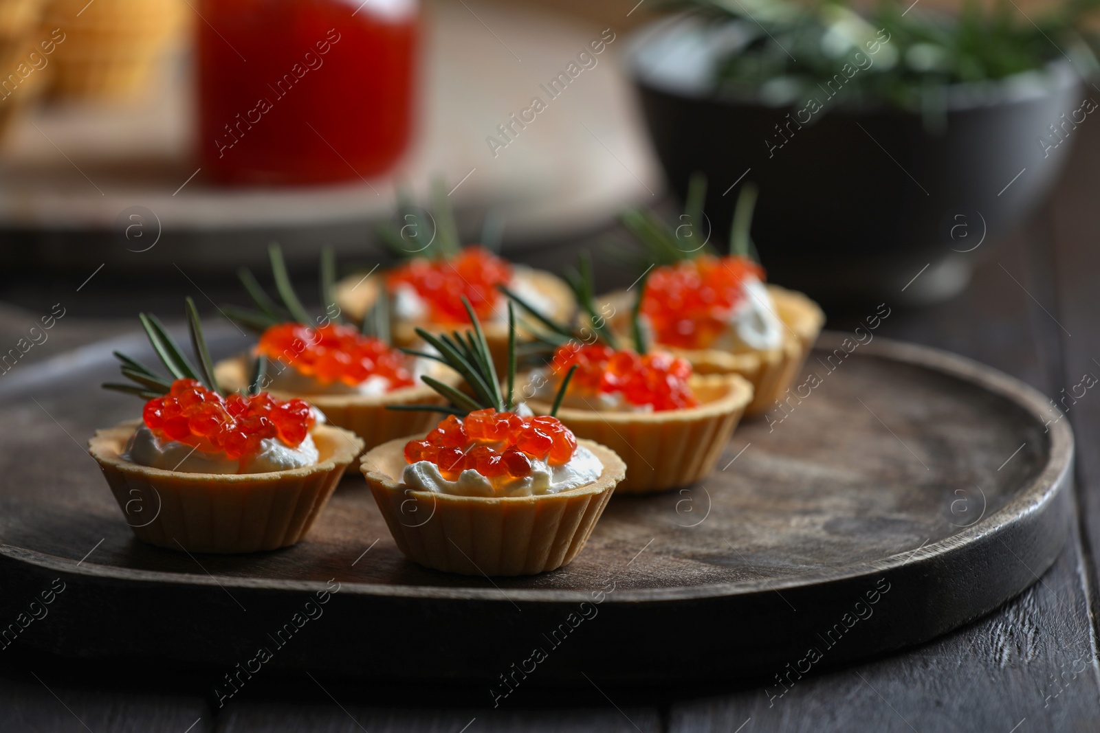 Photo of Delicious tartlets with red caviar and cream cheese served on wooden table, closeup