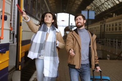 Photo of Being late. Worried couple with suitcase running towards train at station