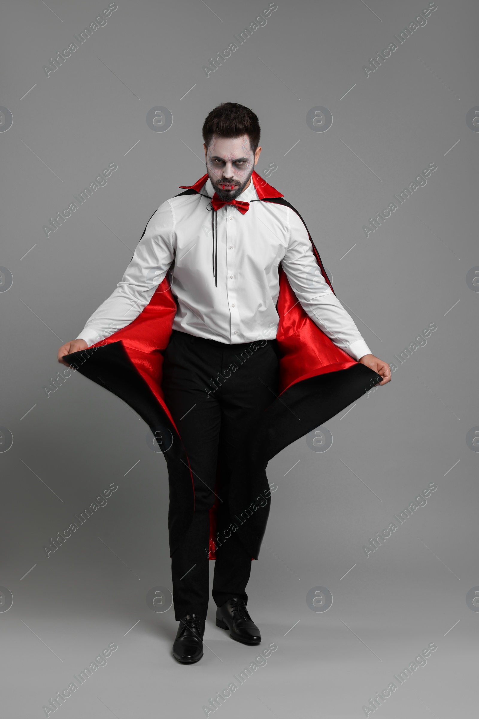 Photo of Man in scary vampire costume with fangs on light grey background. Halloween celebration