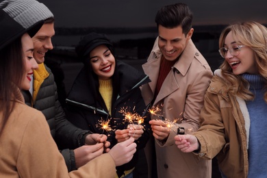 Photo of People in warm clothes holding burning sparklers on dark background