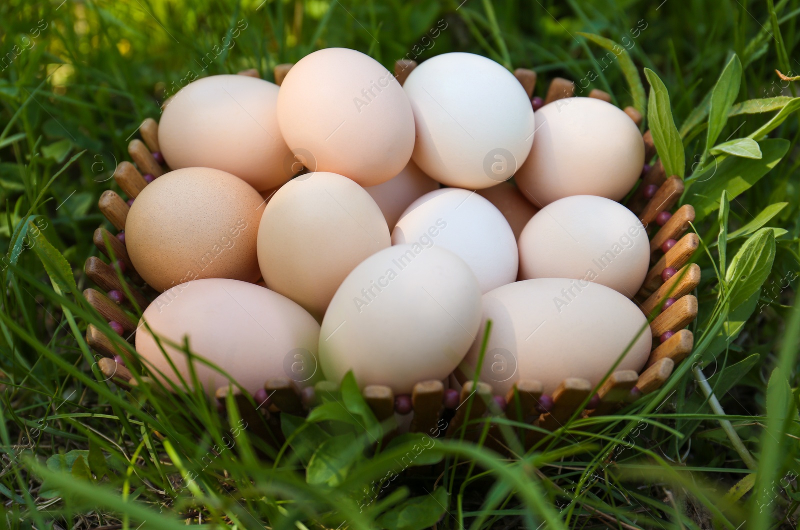 Photo of Fresh raw eggs in wooden basket on green grass, above view