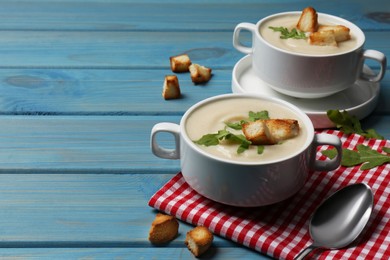 Photo of Bowls with tasty creamy soup of parsnip served on light blue wooden table, space for text
