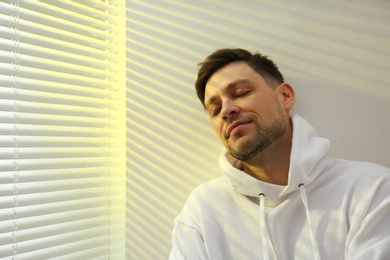 Handsome man near window with Venetian blinds. Space for text