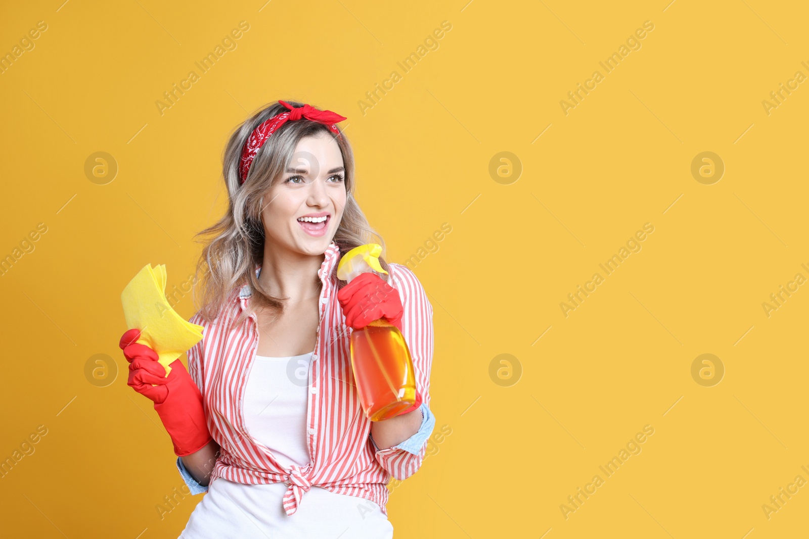 Photo of Beautiful young woman with rag and bottle of detergent singing on orange background. Space for text