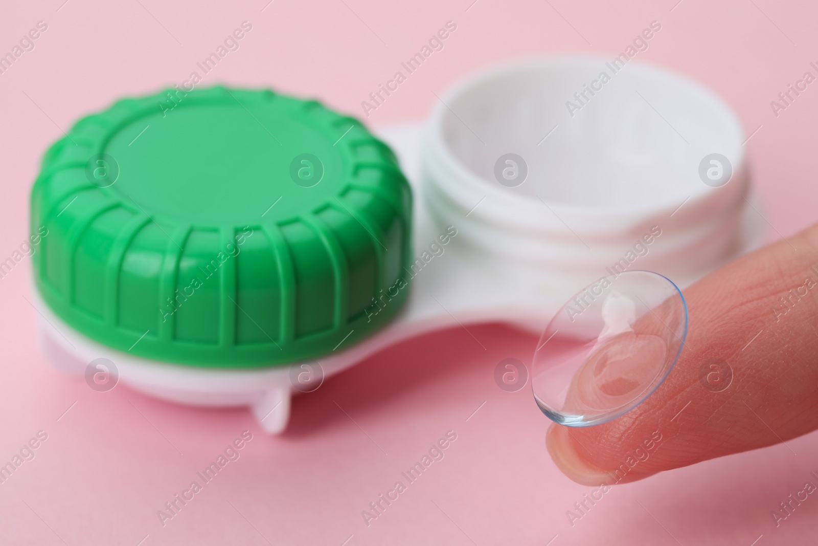 Photo of Woman with contact lens near case on pink background, closeup