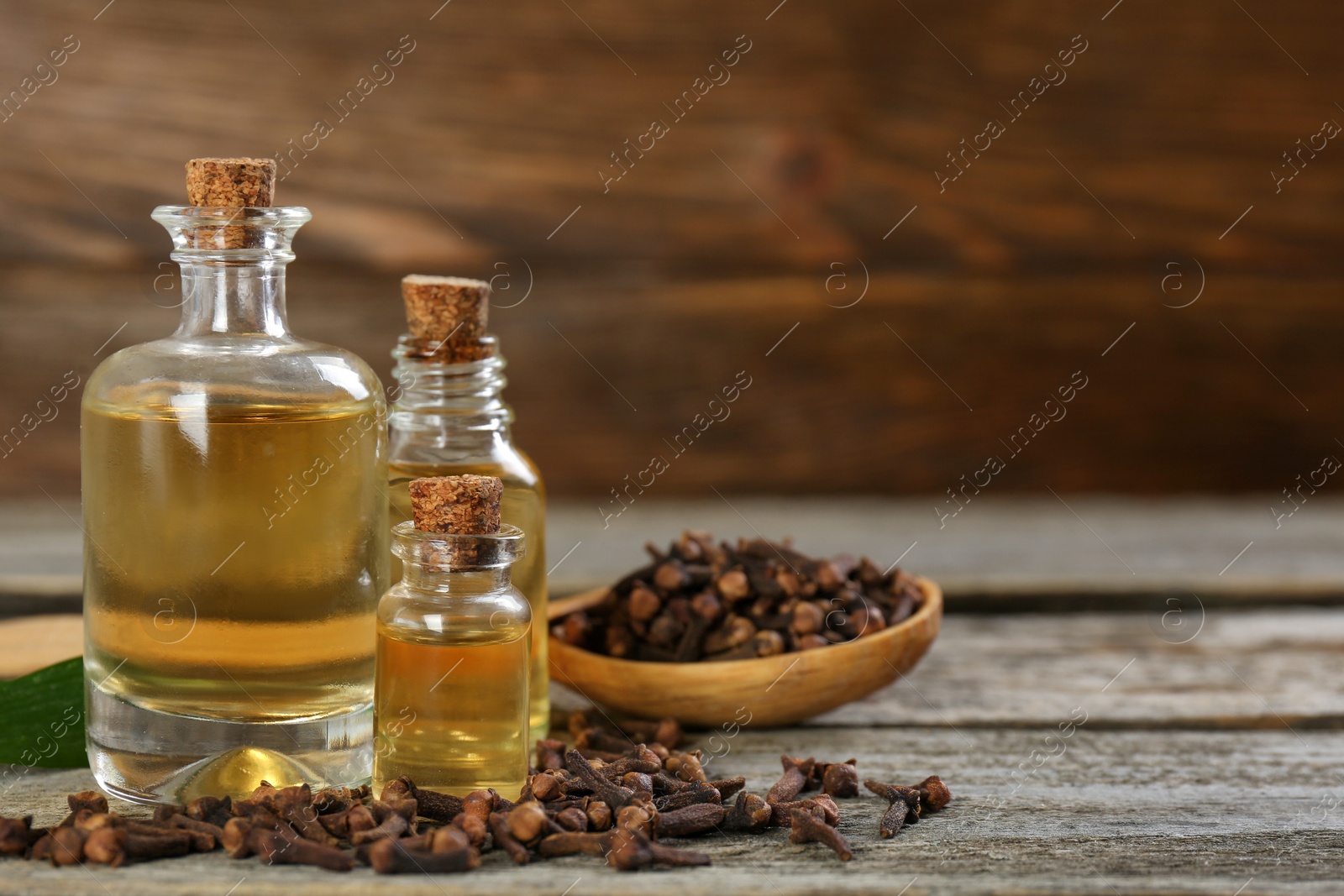 Photo of Essential oil and dried cloves on wooden table. Space for text