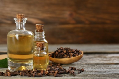 Photo of Essential oil and dried cloves on wooden table. Space for text