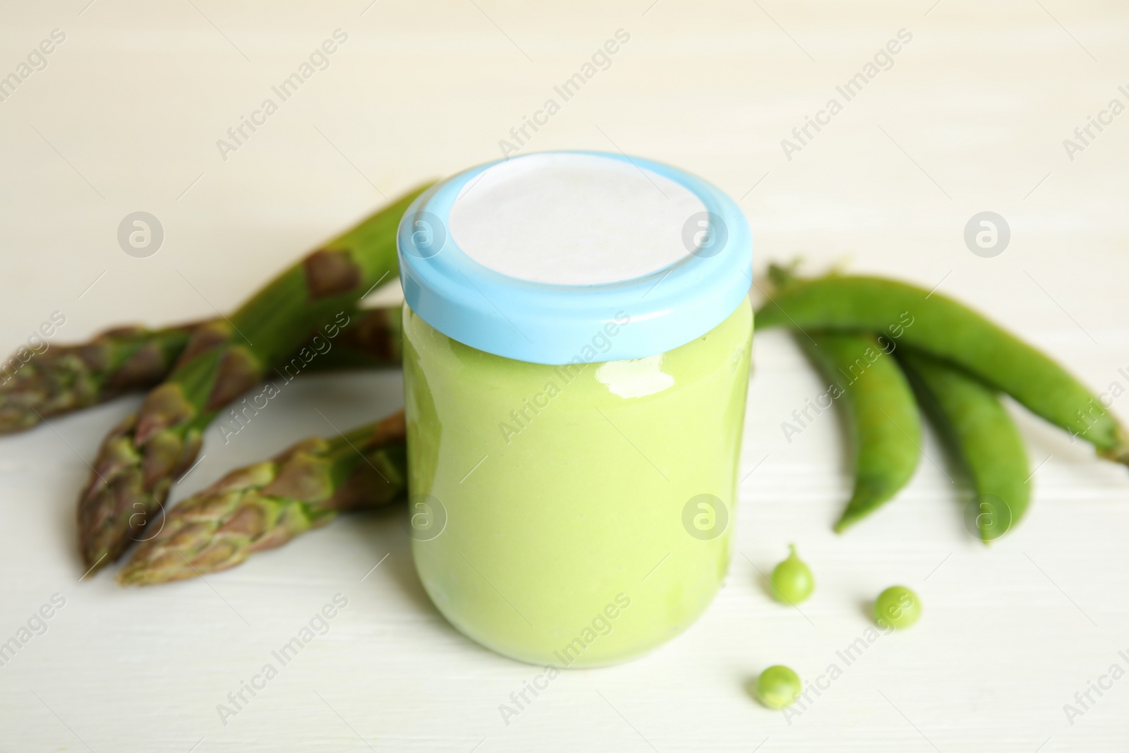 Photo of Jar with baby food, fresh pea pods and asparagus on white wooden table