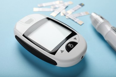 Photo of Digital glucometer, lancet pen and test strips on light blue background. Diabetes control