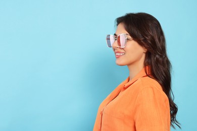 Photo of Happy beautiful woman with stylish sunglasses on light blue background, space for text