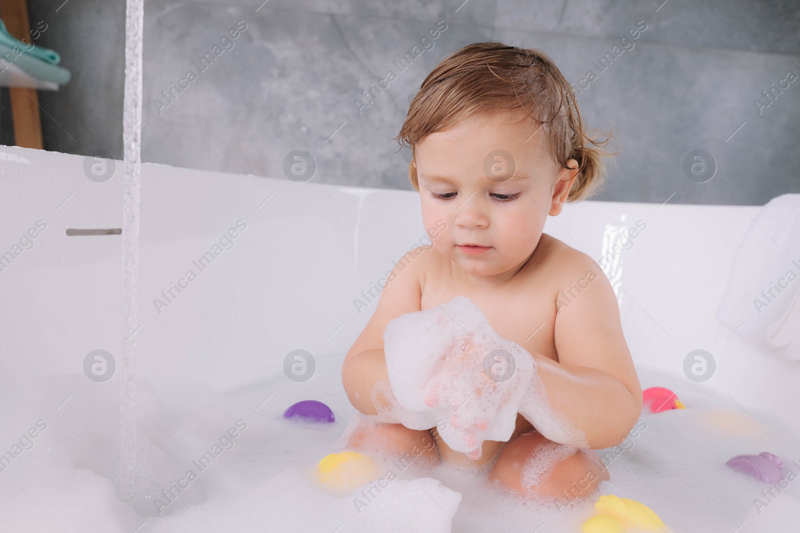 Photo of Cute little girl taking bubble bath with toys indoors