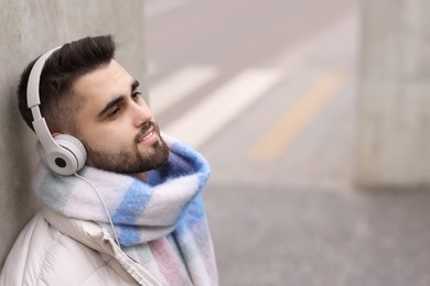 Smiling man in warm scarf and headphones on city street. Space for text