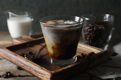 Photo of Glass of delicious iced coffee with milk and beans on wooden table