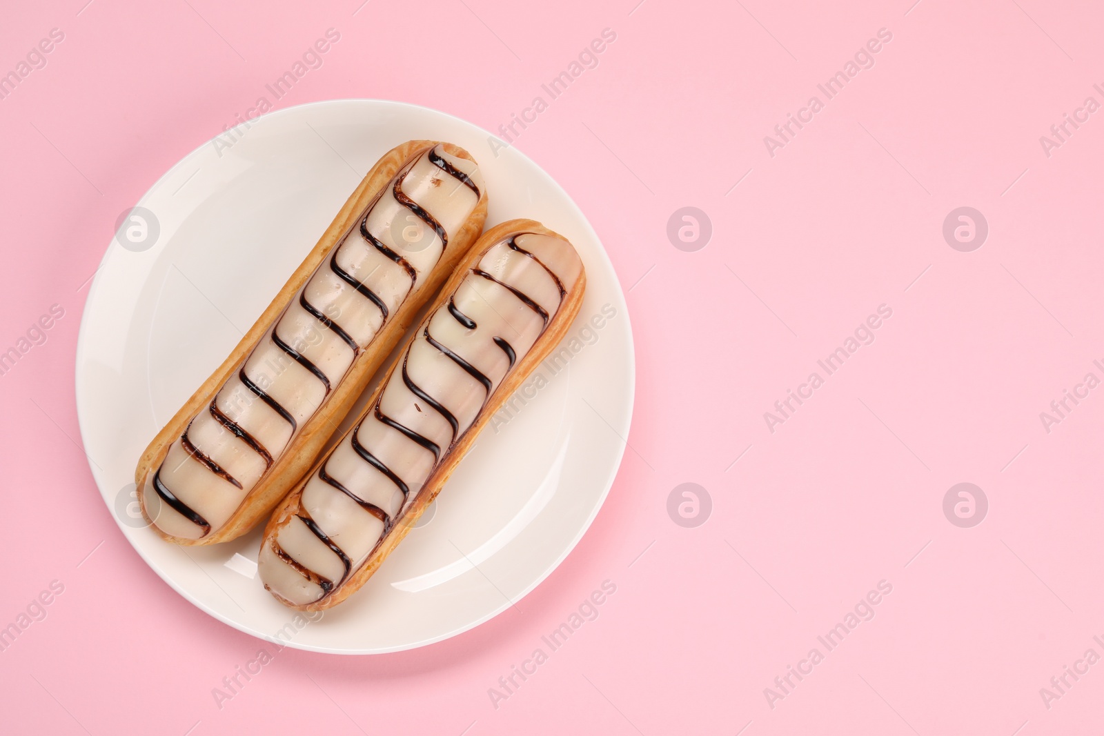 Photo of Delicious eclairs covered with glaze on pink background, top view