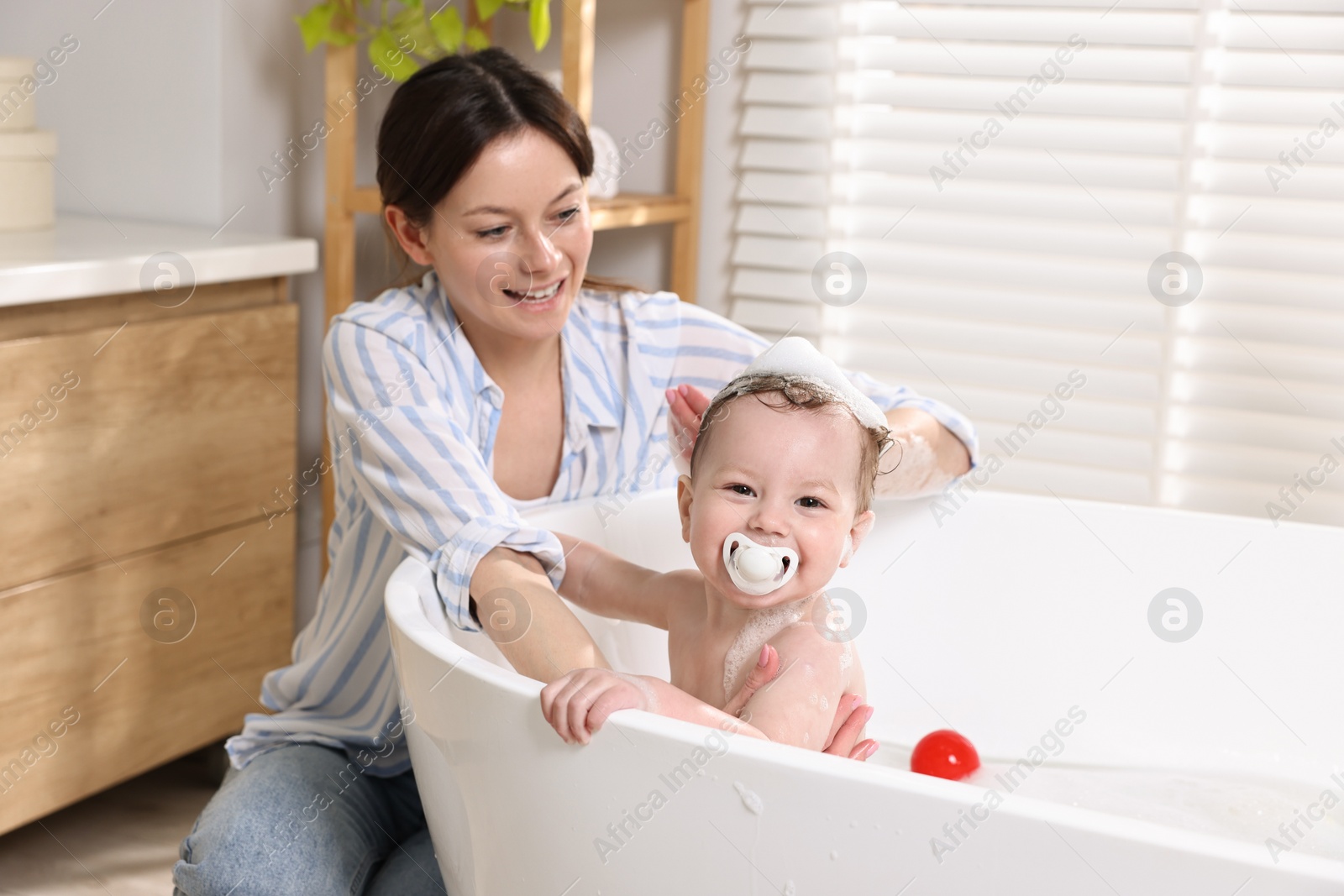 Photo of Mother bathing her cute little baby in tub at home