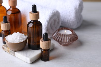 Photo of Essential oils, sea salt, candle and towels on white table, closeup