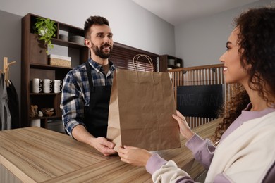 Worker giving paper bag to customer in cafe