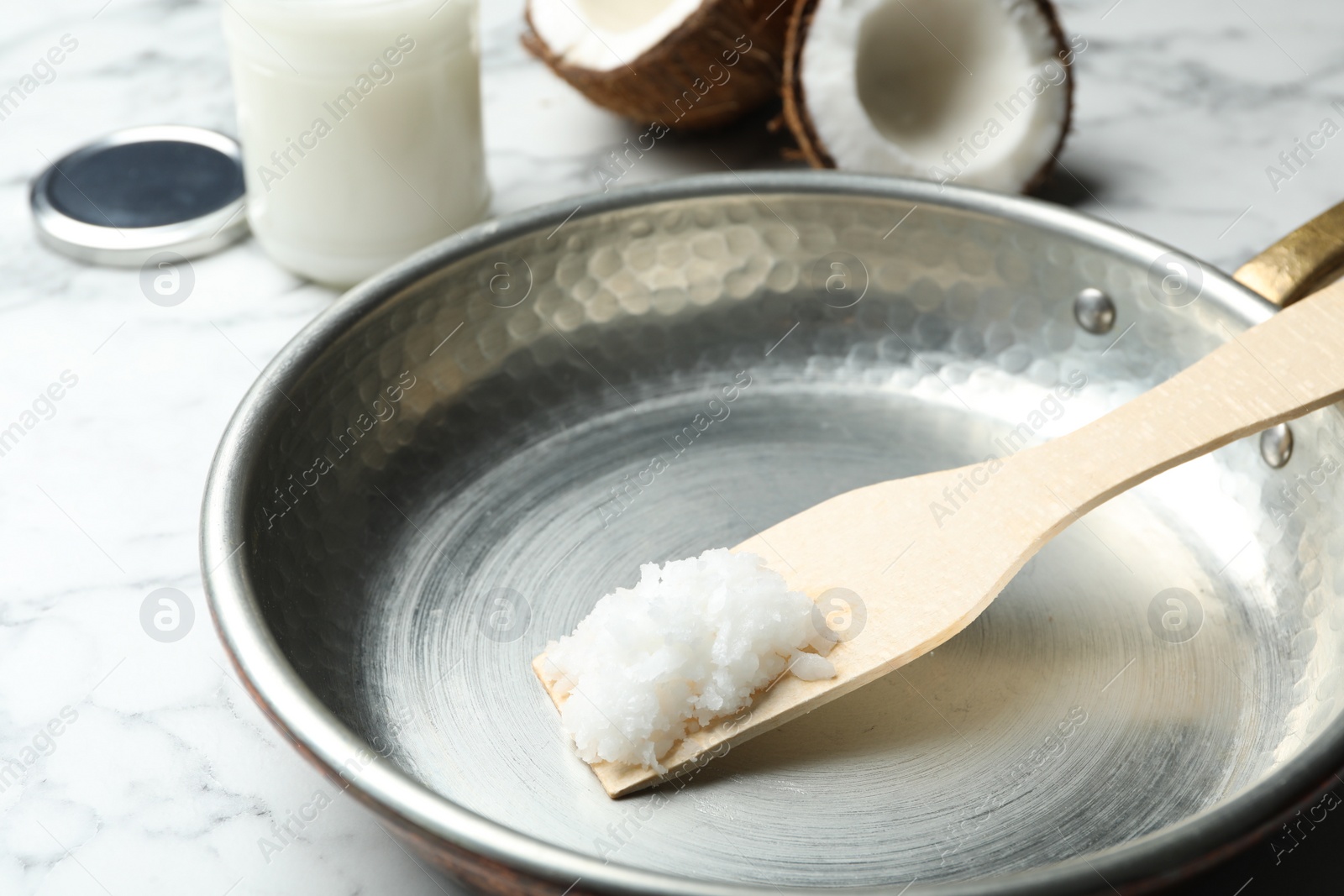 Photo of Frying pan with coconut oil and wooden spatula on white marble table, closeup. Healthy cooking