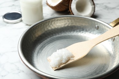 Frying pan with coconut oil and wooden spatula on white marble table, closeup. Healthy cooking