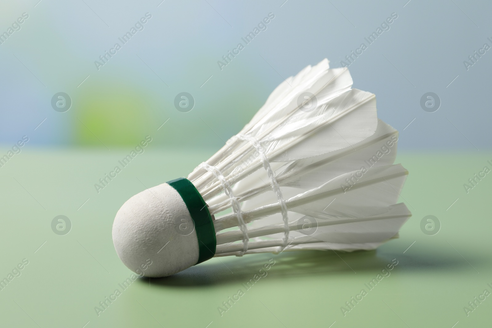 Photo of Feather badminton shuttlecock on green table against blurred background, closeup