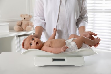 Photo of Doctor weighing cute baby in clinic, closeup