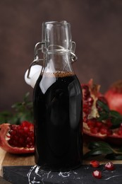 Photo of Tasty pomegranate sauce in bottle, fruits and branches on table, closeup