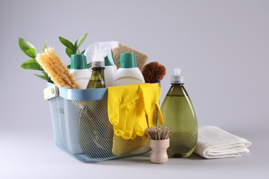 Set of different cleaning supplies in basket on light grey background