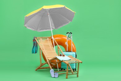 Photo of Deck chair, umbrella, suitcase and beach accessories against green background. Summer vacation