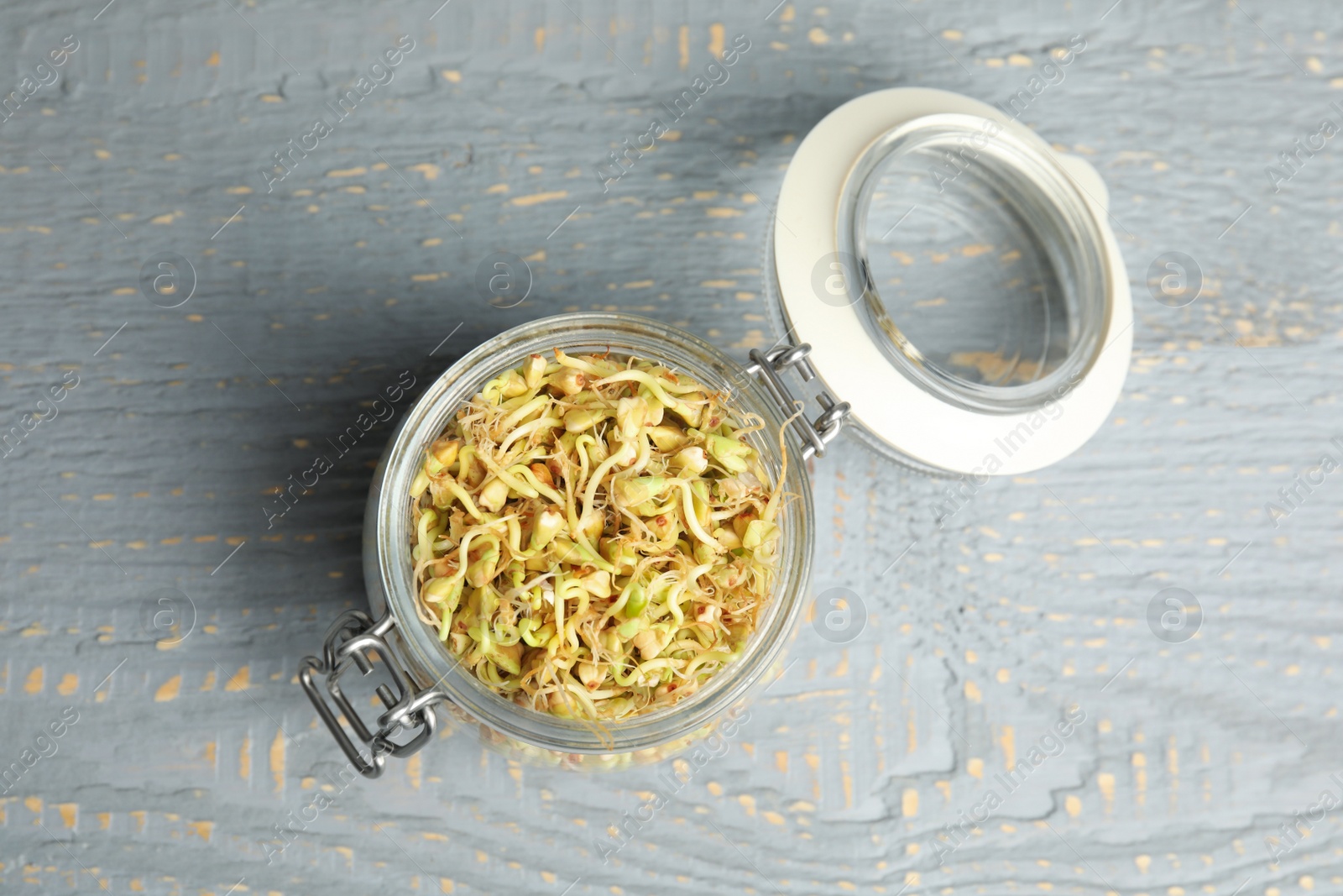 Photo of Glass jar with sprouted green buckwheat on grey wooden table, top view