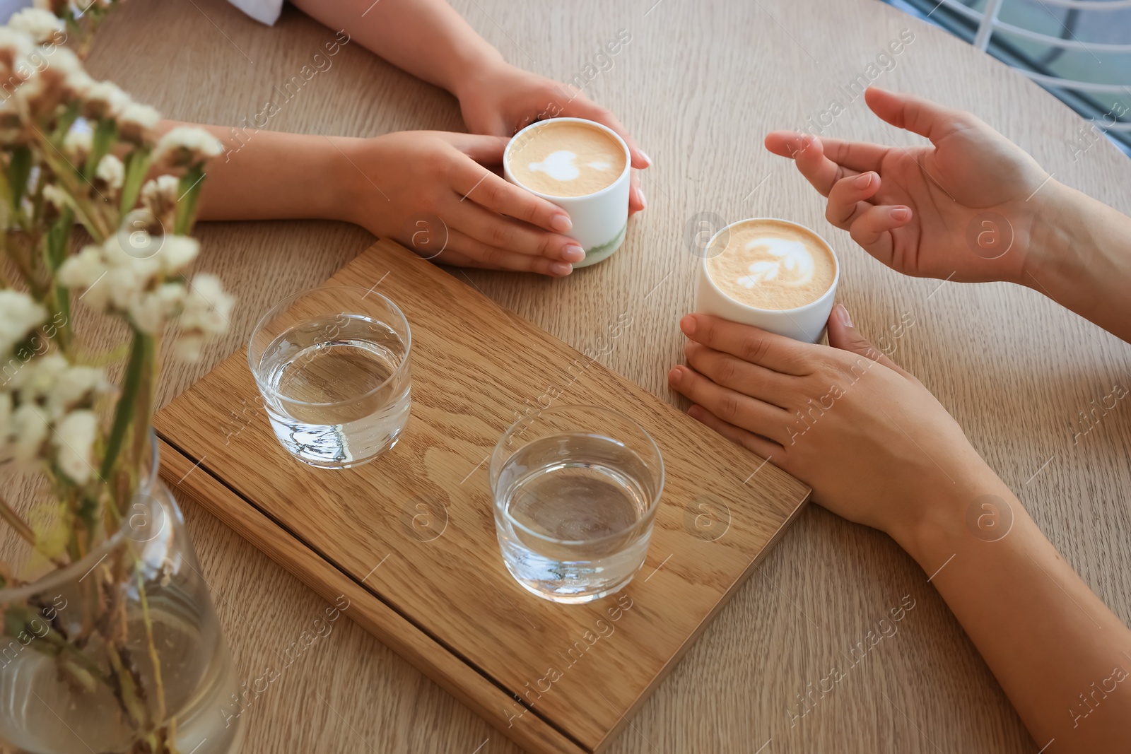 Photo of Friends drinking coffee at wooden table in cafe, closeup