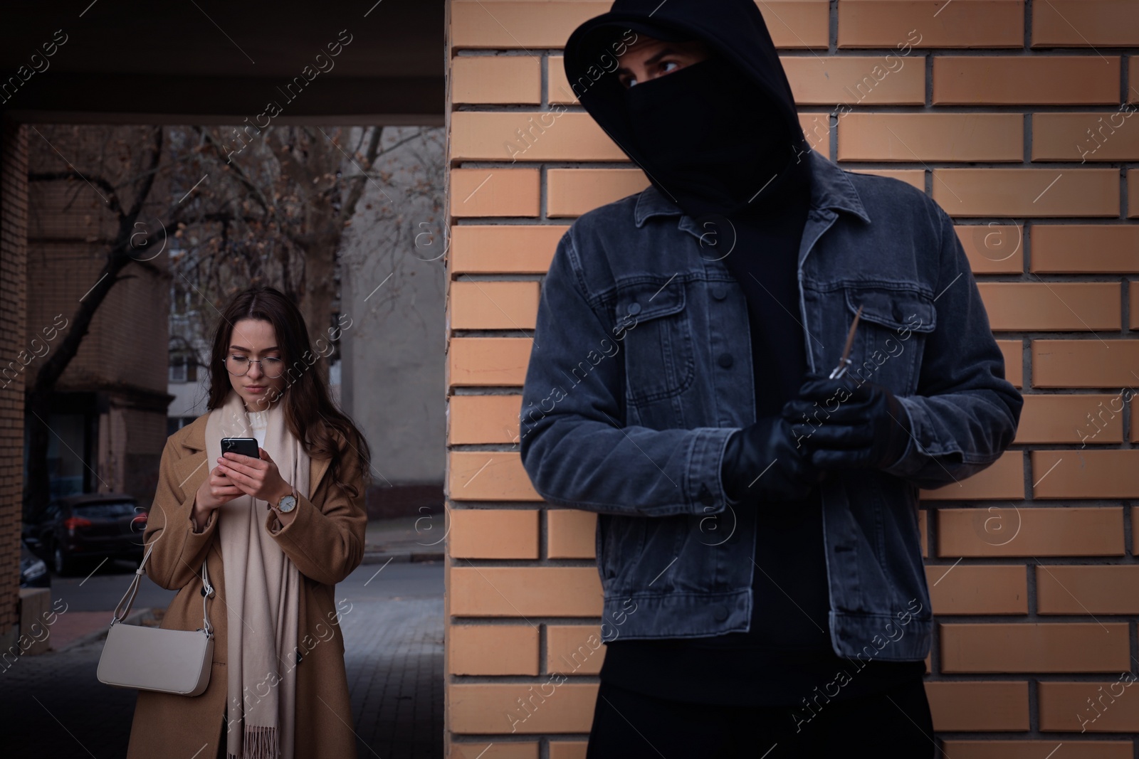 Photo of Criminal with knife hiding behind wall and waiting for victim near alley