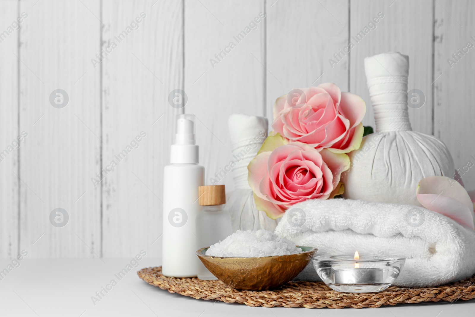 Photo of Composition with different spa products, candle and roses on white table against wooden background. Space for text