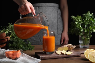 Photo of Woman pouring carrot juice from jug into glass at wooden table, closeup