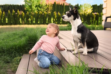 Photo of Adorable baby and furry little dog on wooden porch outdoors