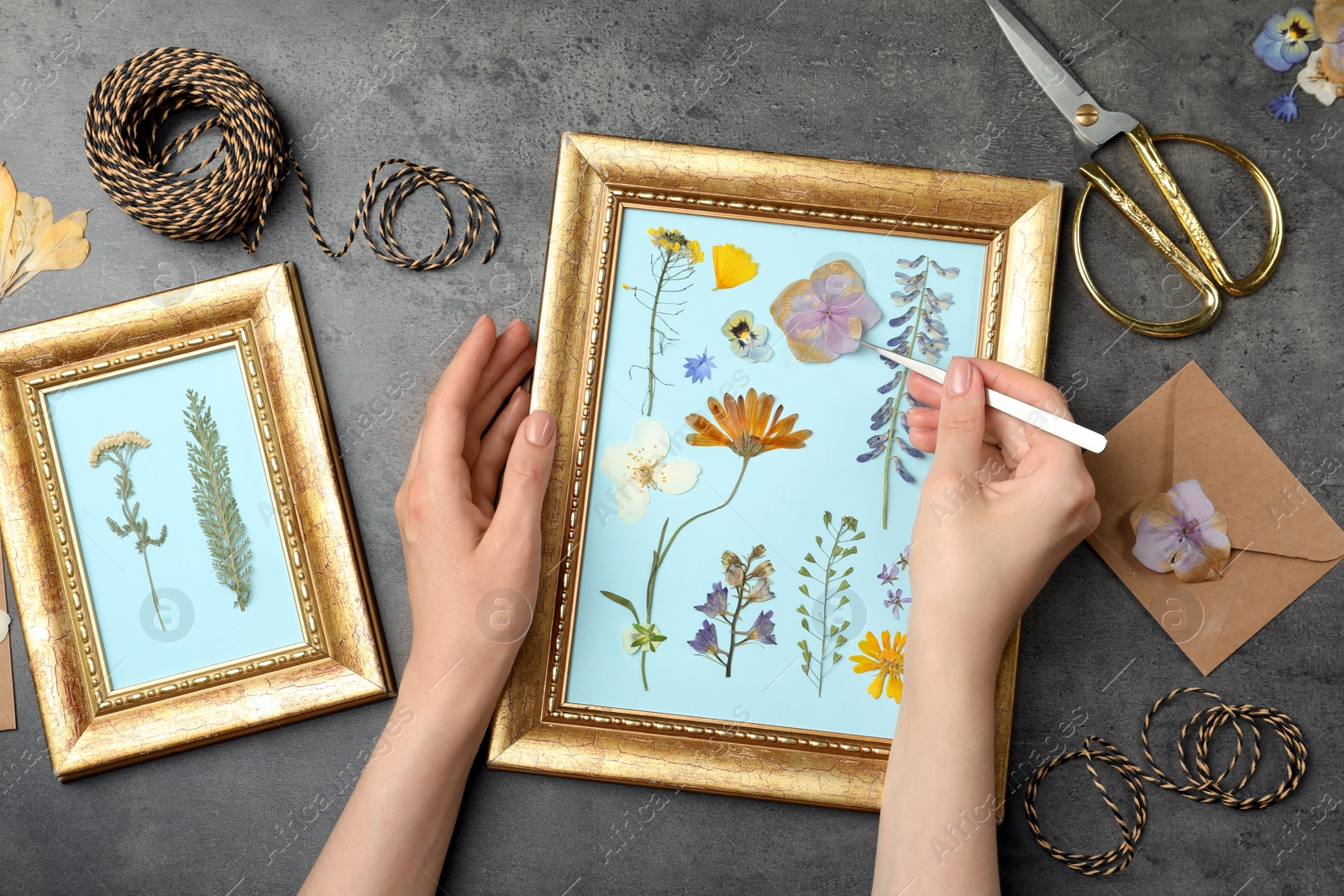 Photo of Woman making beautiful herbarium with pressed dried flower at black table, top view