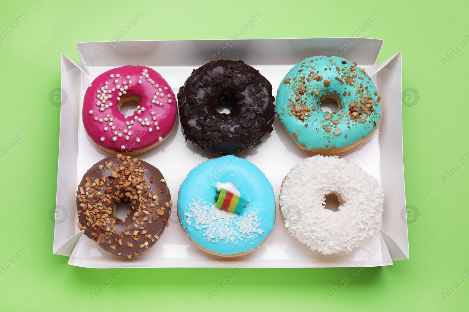 Photo of Box with different tasty glazed donuts on light green background, top view