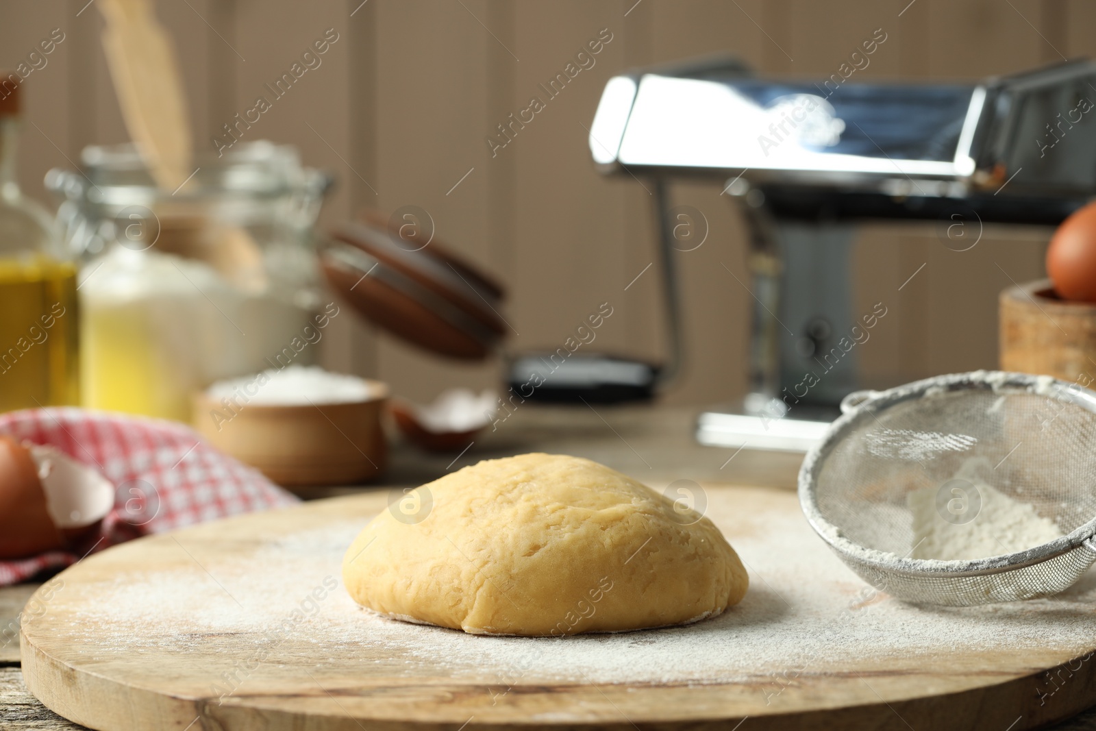 Photo of Raw dough for pasta, sieve and flour on table, closeup