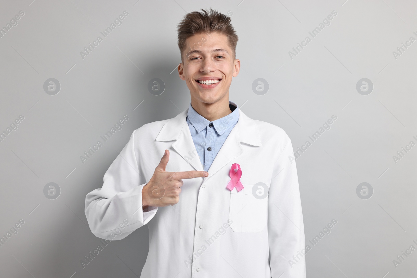 Photo of Mammologist pointing at pink ribbon on light grey background. Breast cancer awareness