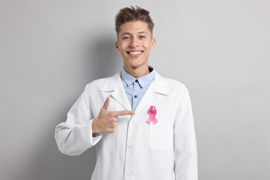 Mammologist pointing at pink ribbon on light grey background. Breast cancer awareness