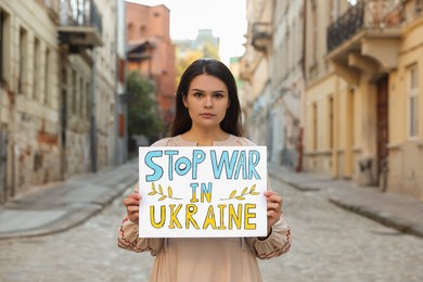 Sad woman holding poster Stop War in Ukraine on city street