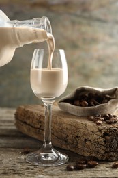 Pouring coffee cream liqueur into glass at wooden table, closeup