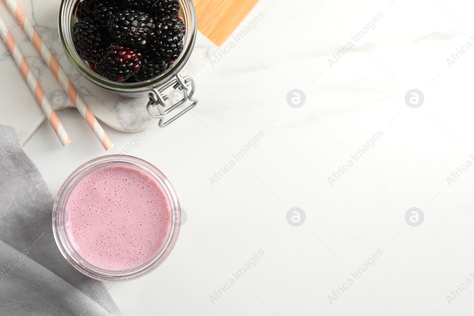 Photo of Glass of blackberry smoothie and berries on white table, flat lay. Space for text