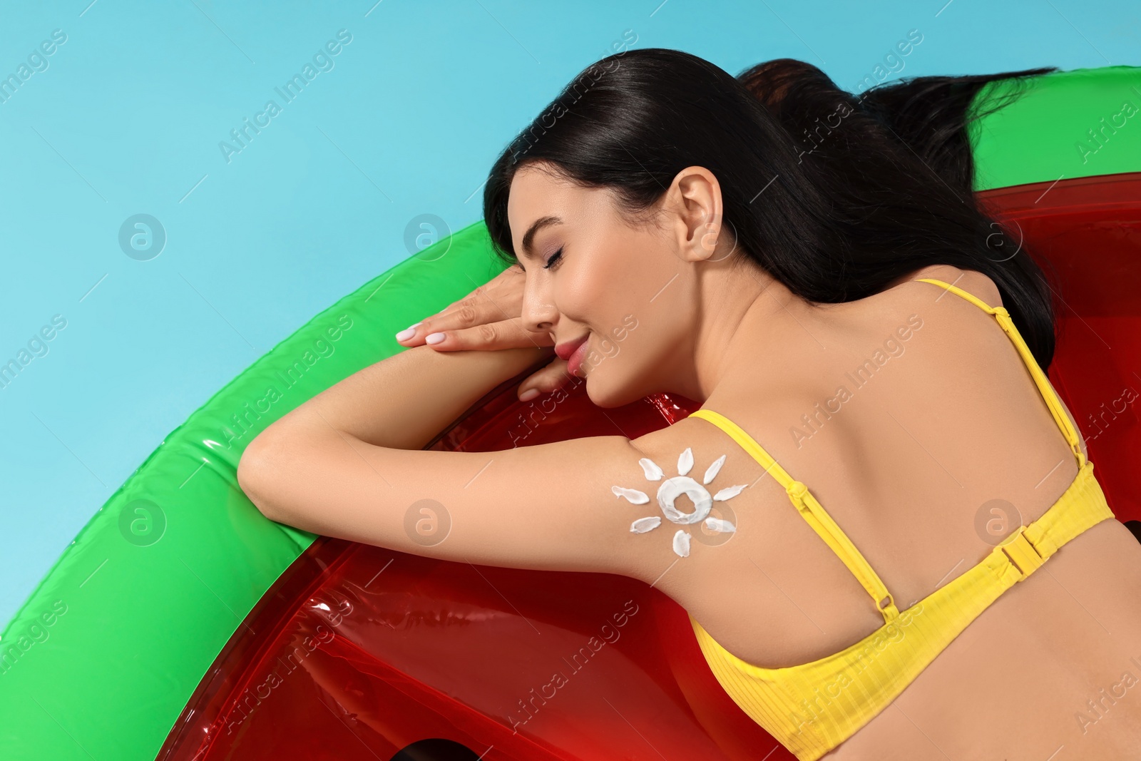 Photo of Young woman with sun protection cream on inflatable mattress against light blue background