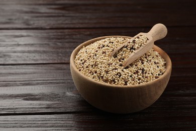 Photo of Raw quinoa seeds and scoop in bowl on wooden table, closeup. Space for text